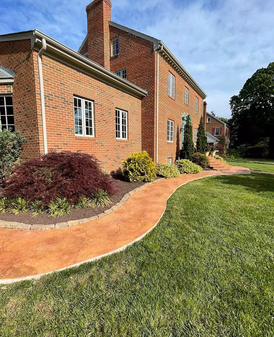 Curved stone-edged walkway and fresh mulch beds along a brick home beside a striped lawn