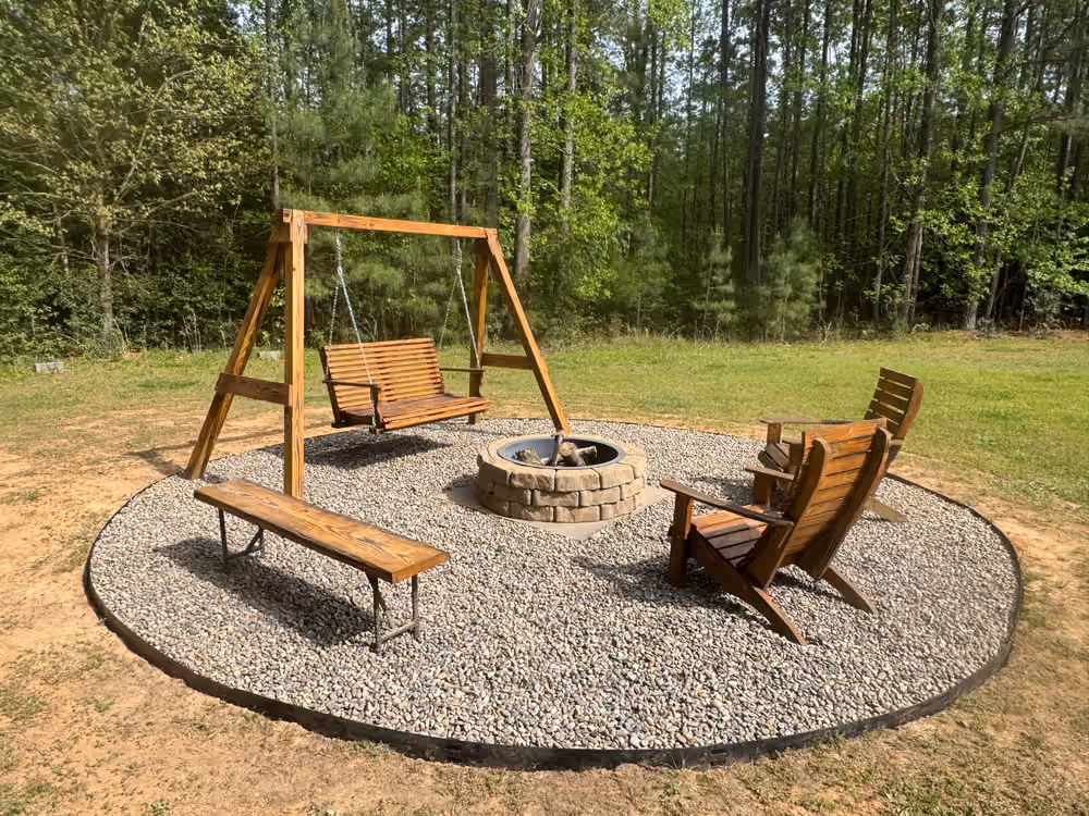 Circular gravel seating area with a stone fire pit, wooden swing and Adirondack chairs