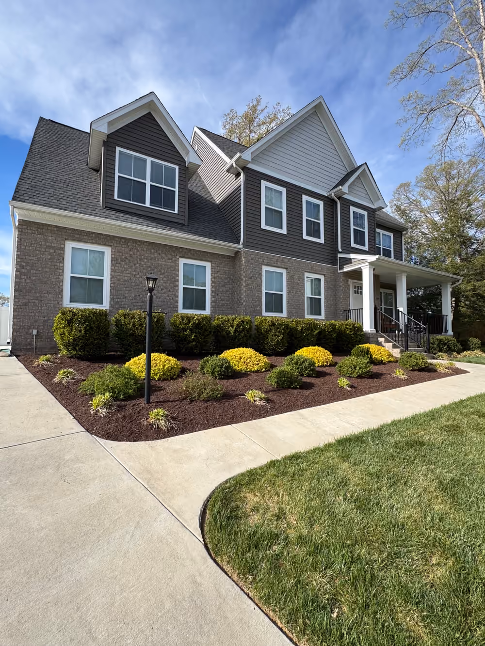 Front-yard foundation beds with fresh dark mulch and shaped shrubs along a walkway