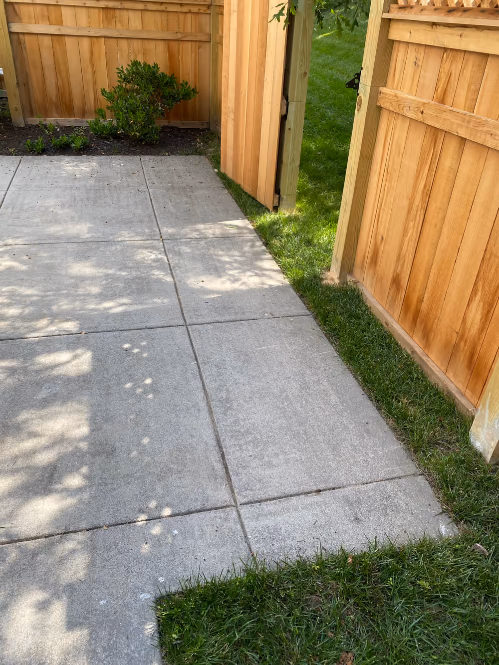 Cracked concrete patio slabs beside a wooden fence before removal