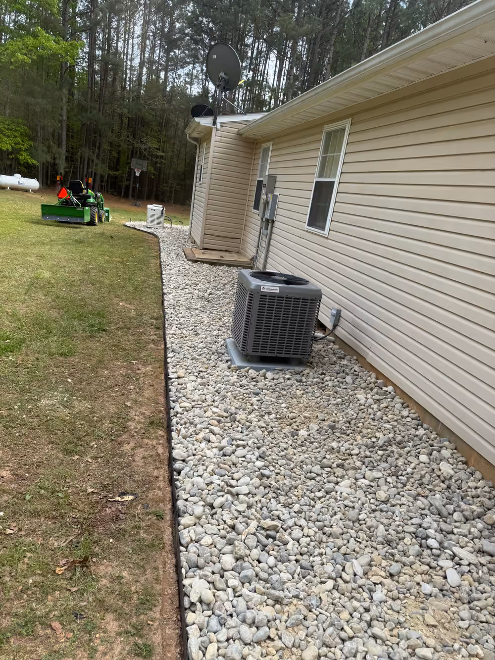 River rock bed with clean steel edging along a house foundation and AC unit